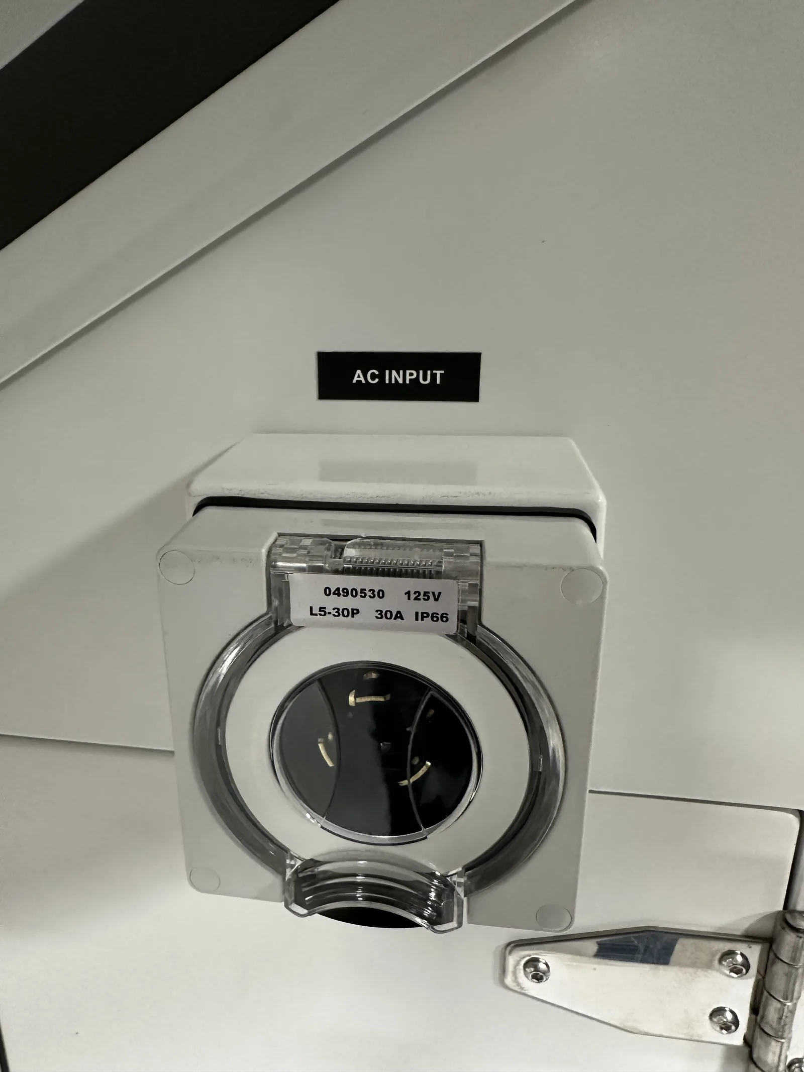 The AC INPUT inlet on the cabinet: a 30 A twist-lock socket under a flip cover